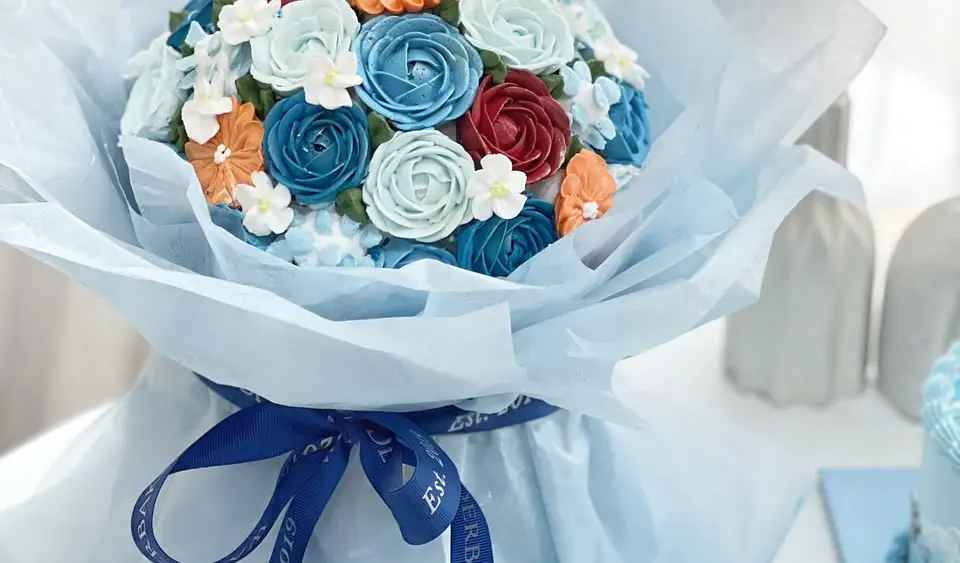 Bouquet cake bunga buttercream biru, putih, oranye dan merah dengan pita Wanderbakes